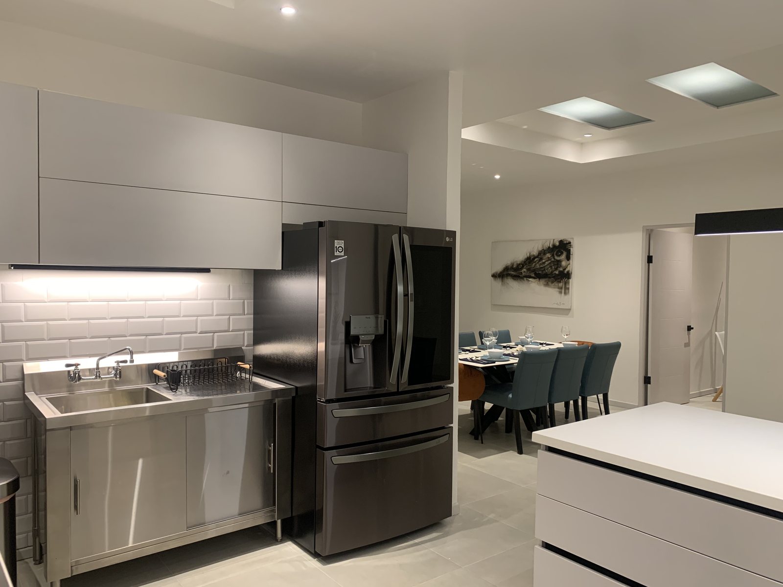 Kitchen with white cabinets, a black French-door fridge and a stainless sink, looking through to the dining room