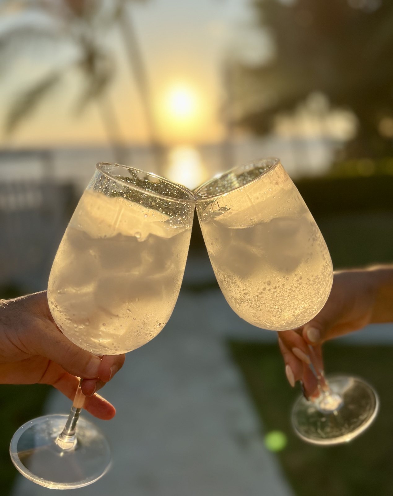 Two glasses clinking against an orange sunset sky over the ocean