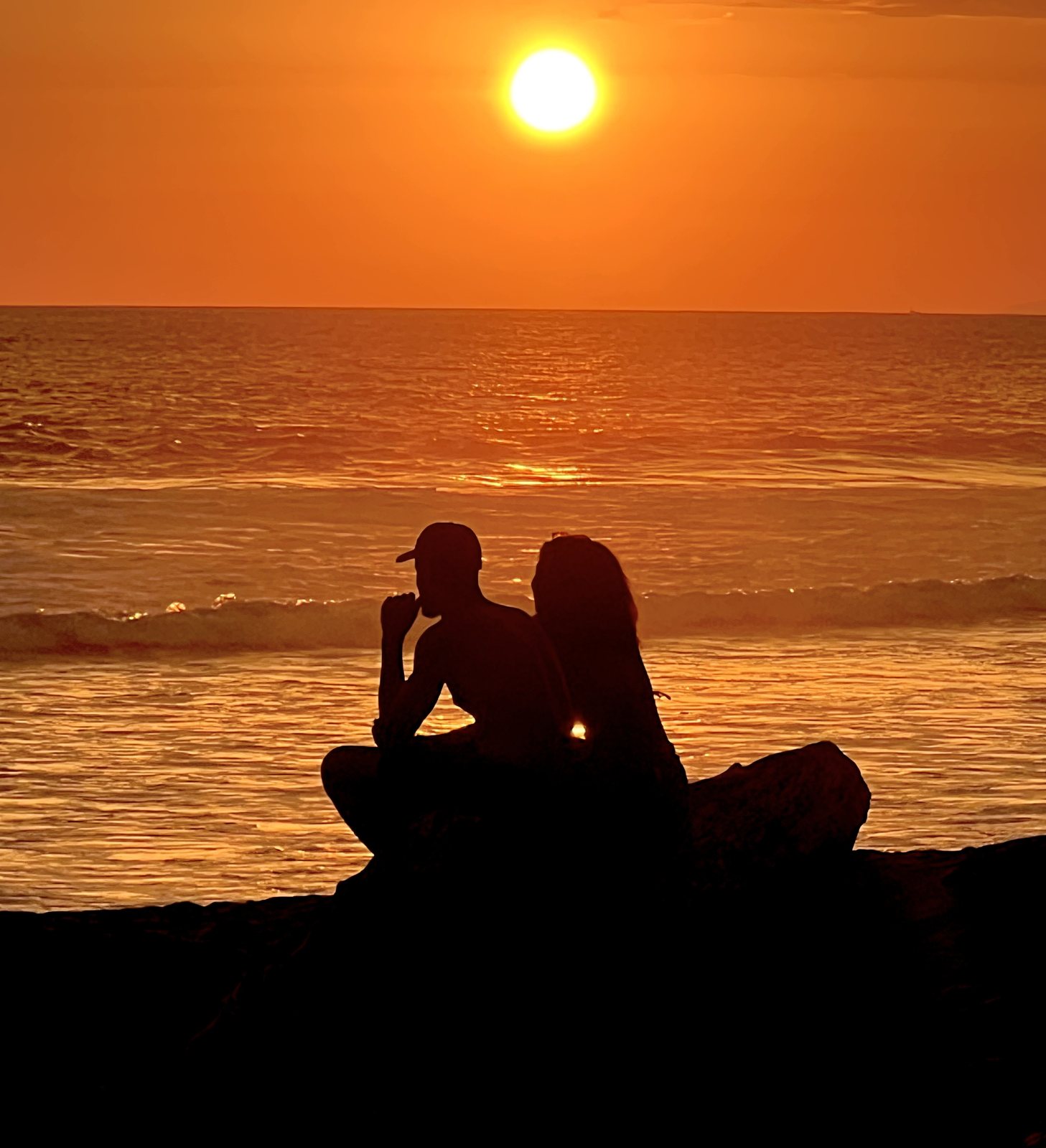 Couple silhouetted on the black-sand beach as the sun sets over the Pacific at Playa Hermosa